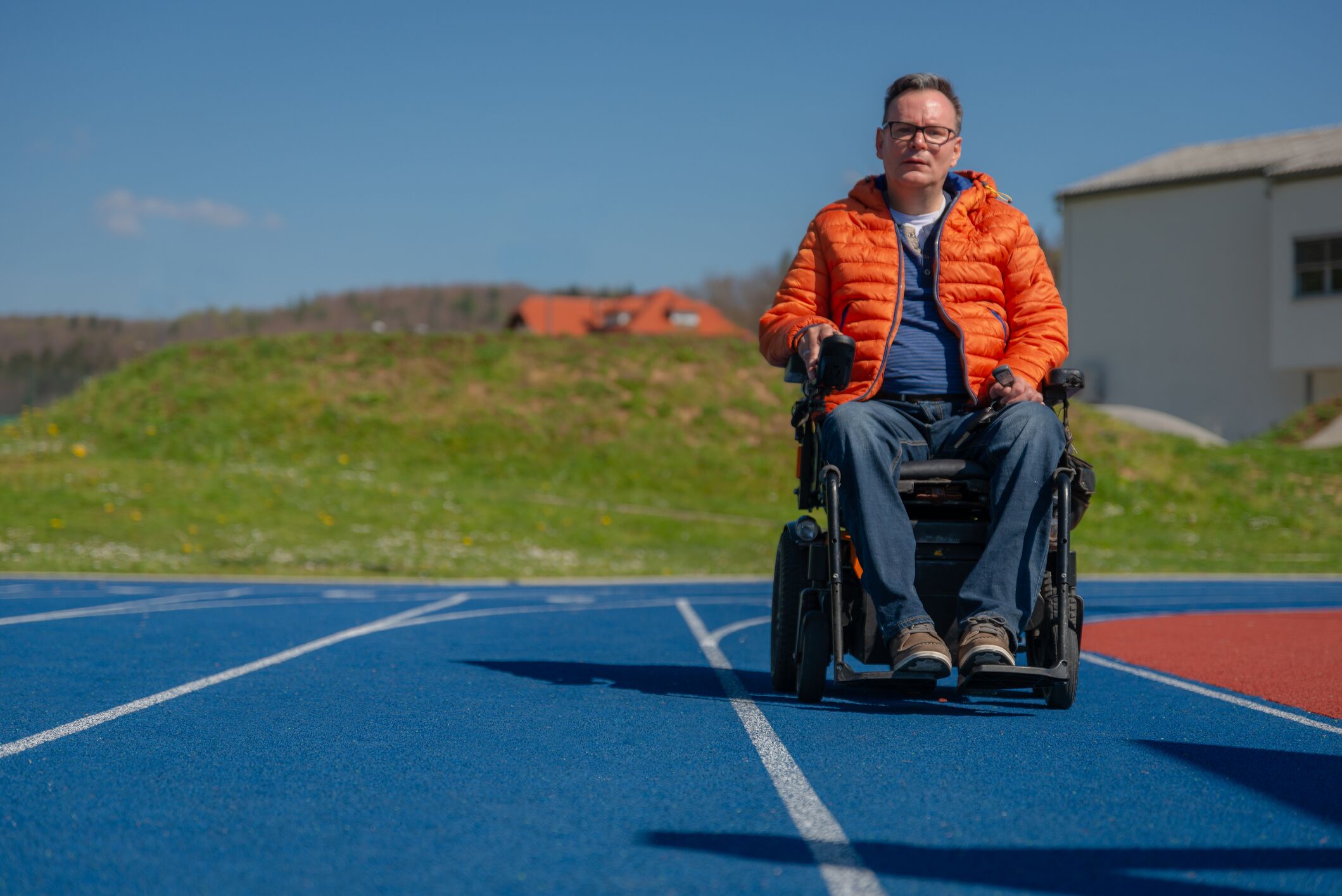 A disabled man in a motorized wheelchair nostalgically on a blue treadmill on a sports field. consumables